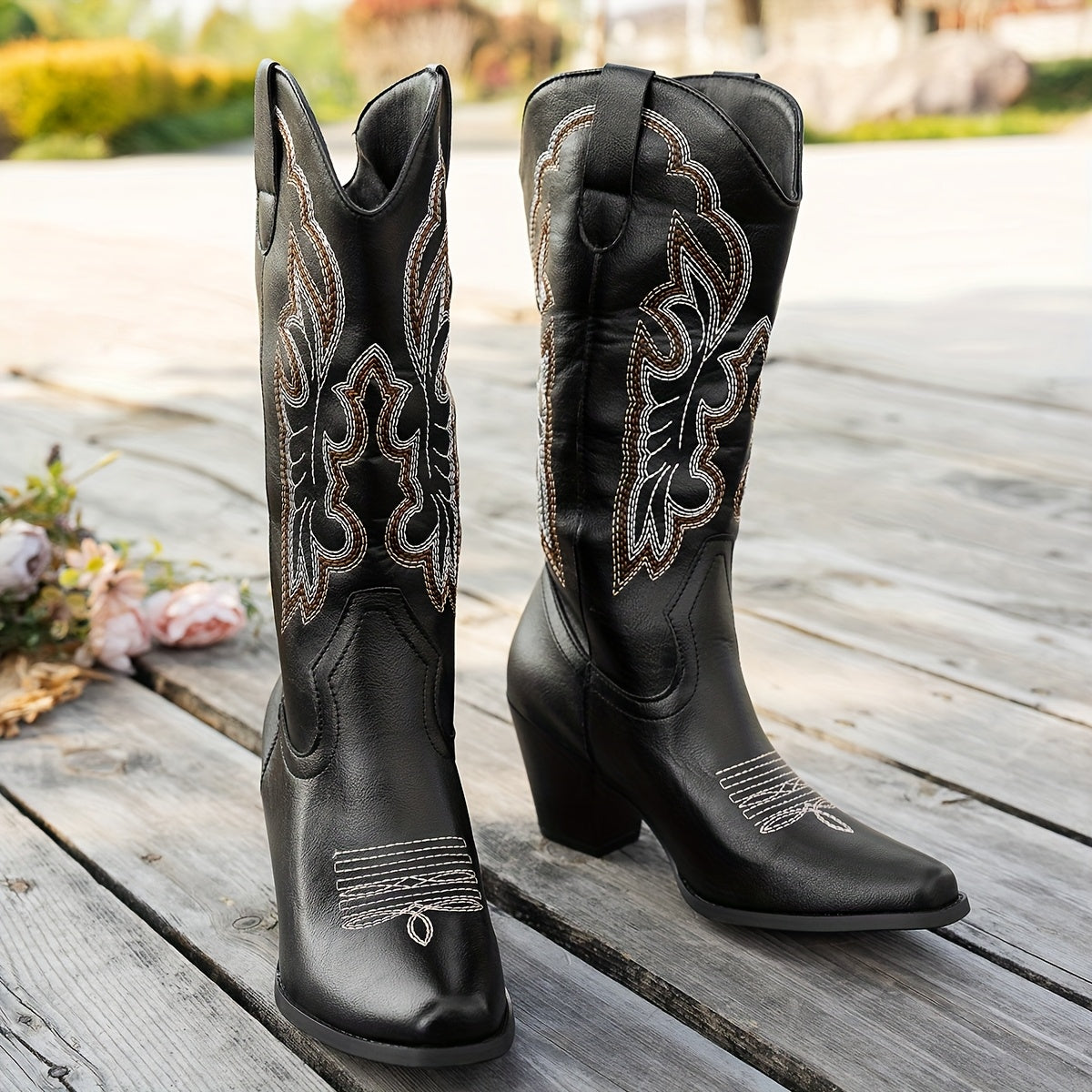 Black cowboy boots with intricate designs on a wooden surface